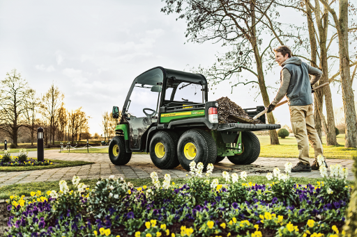 A man shoveling dirt into the bed of a John Deere® UTV sitting on a side walk.
